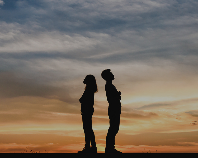 Silhouette of couple standing back to back in from of a sunset.
